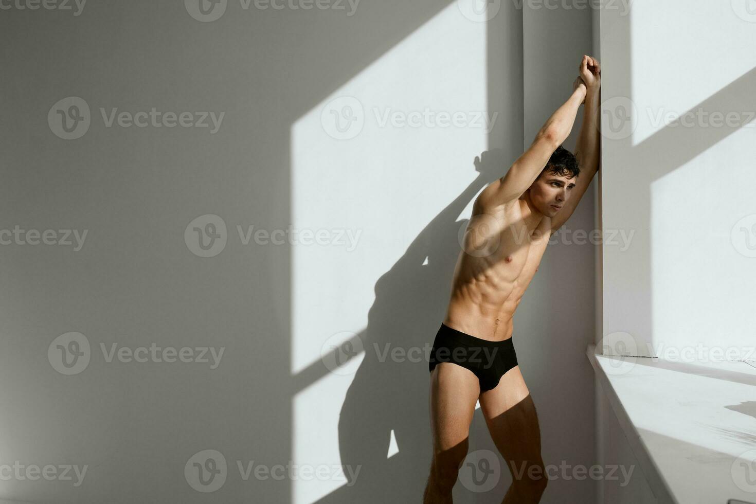 desportivo homem dentro Preto calção com uma bombeado corpo posando luz fundo foto