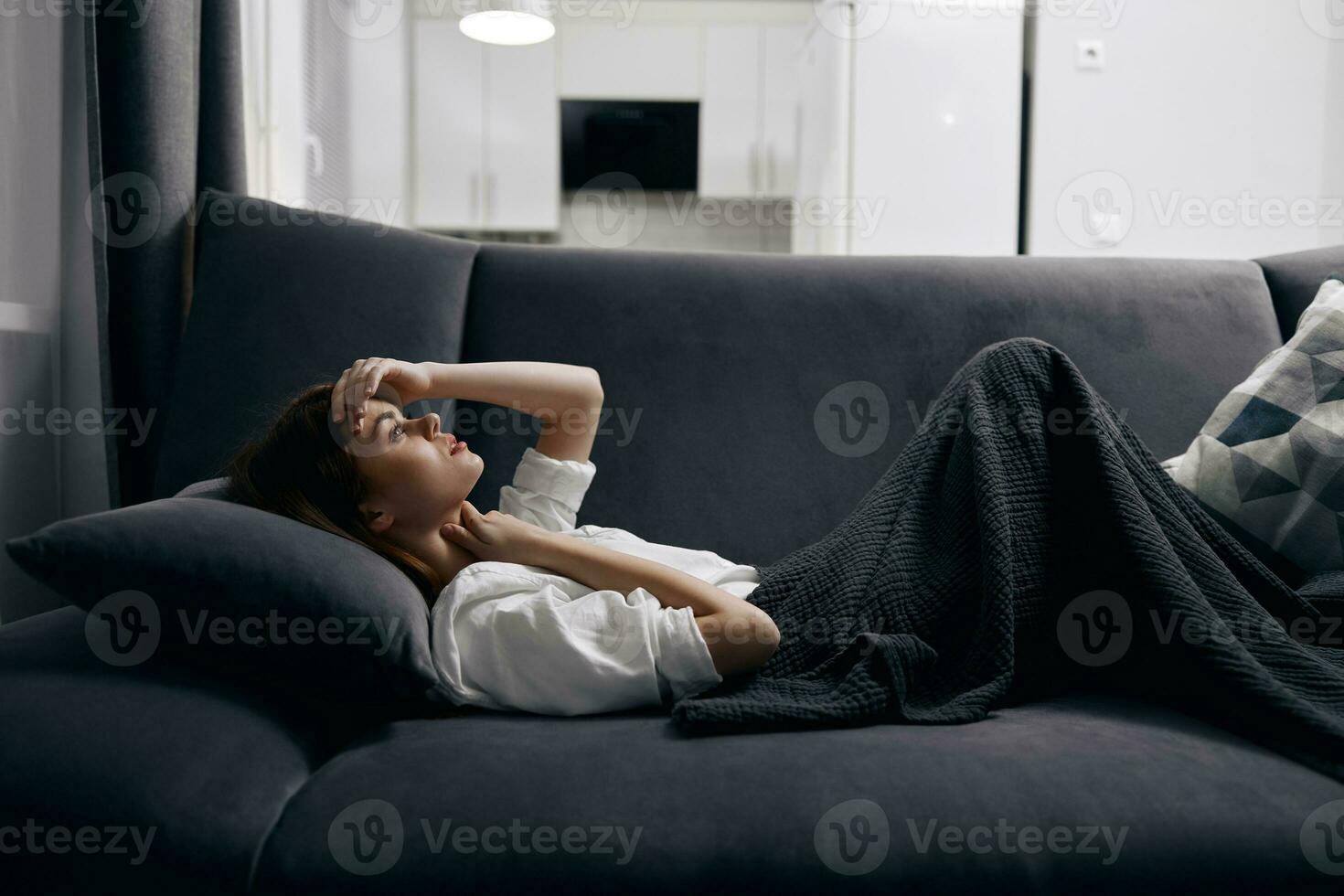 uma mulher dentro uma confortável quarto mentiras em uma sofá coberto com uma cinzento cobertor foto