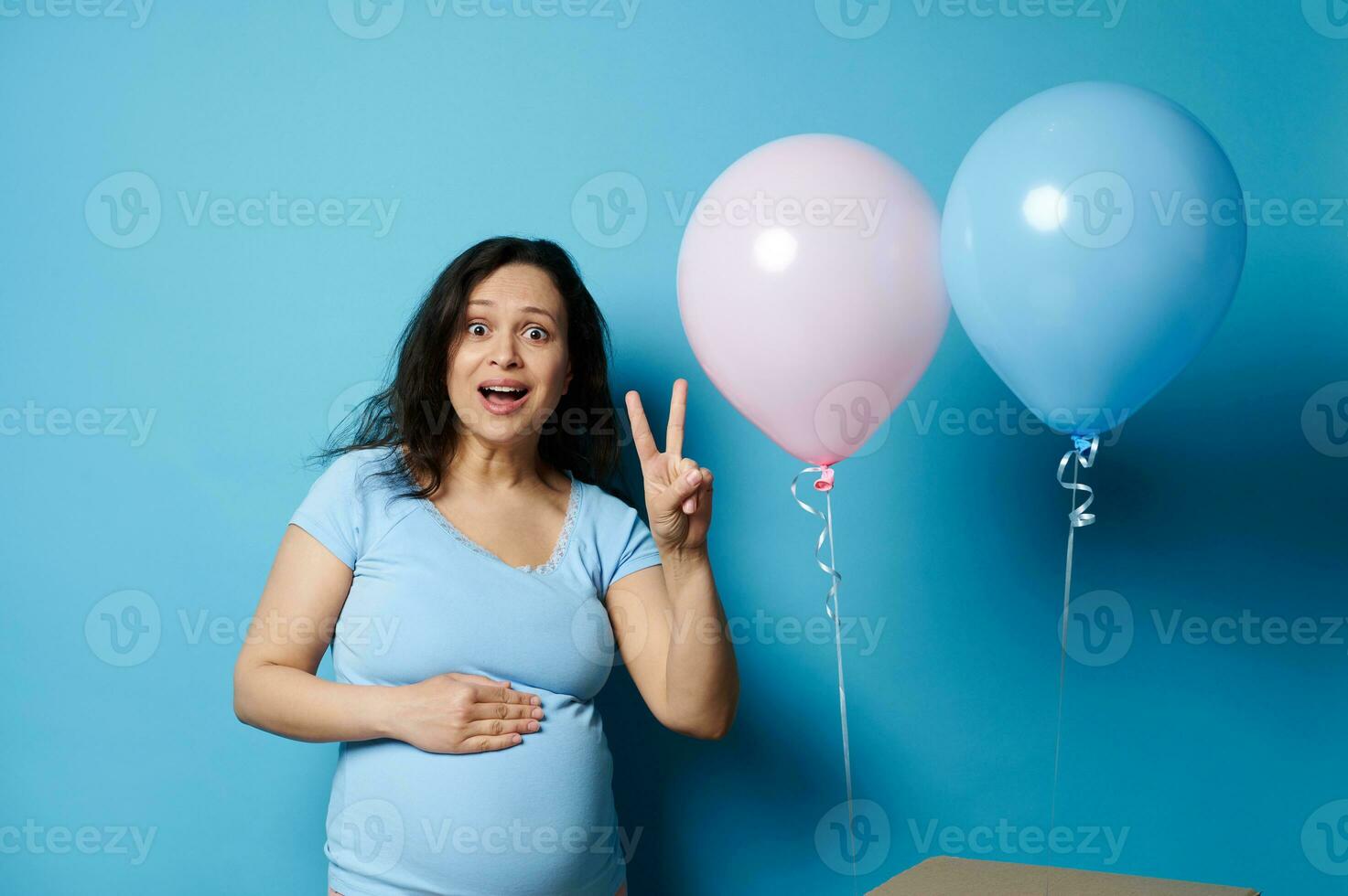 grávida mulher mãe fazendo carinho barriga, mostrando dois dedos, expressando espanto às gênero revelar Festa. esperando gêmeos foto