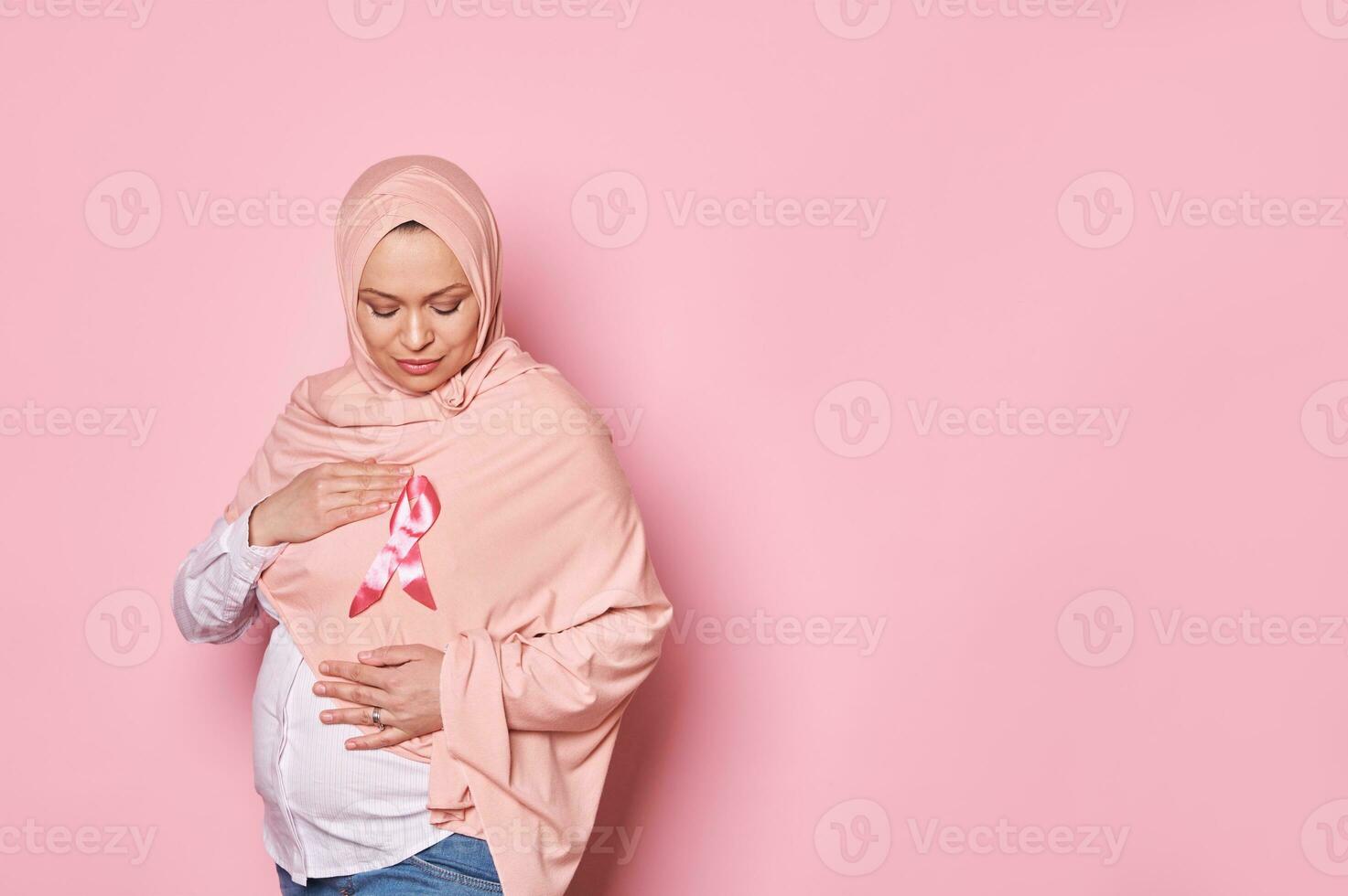 Oriente médio muçulmano grávida mulher, segurando mãos por aí uma Rosa cetim consciência fita em hijab, isolado fundo foto