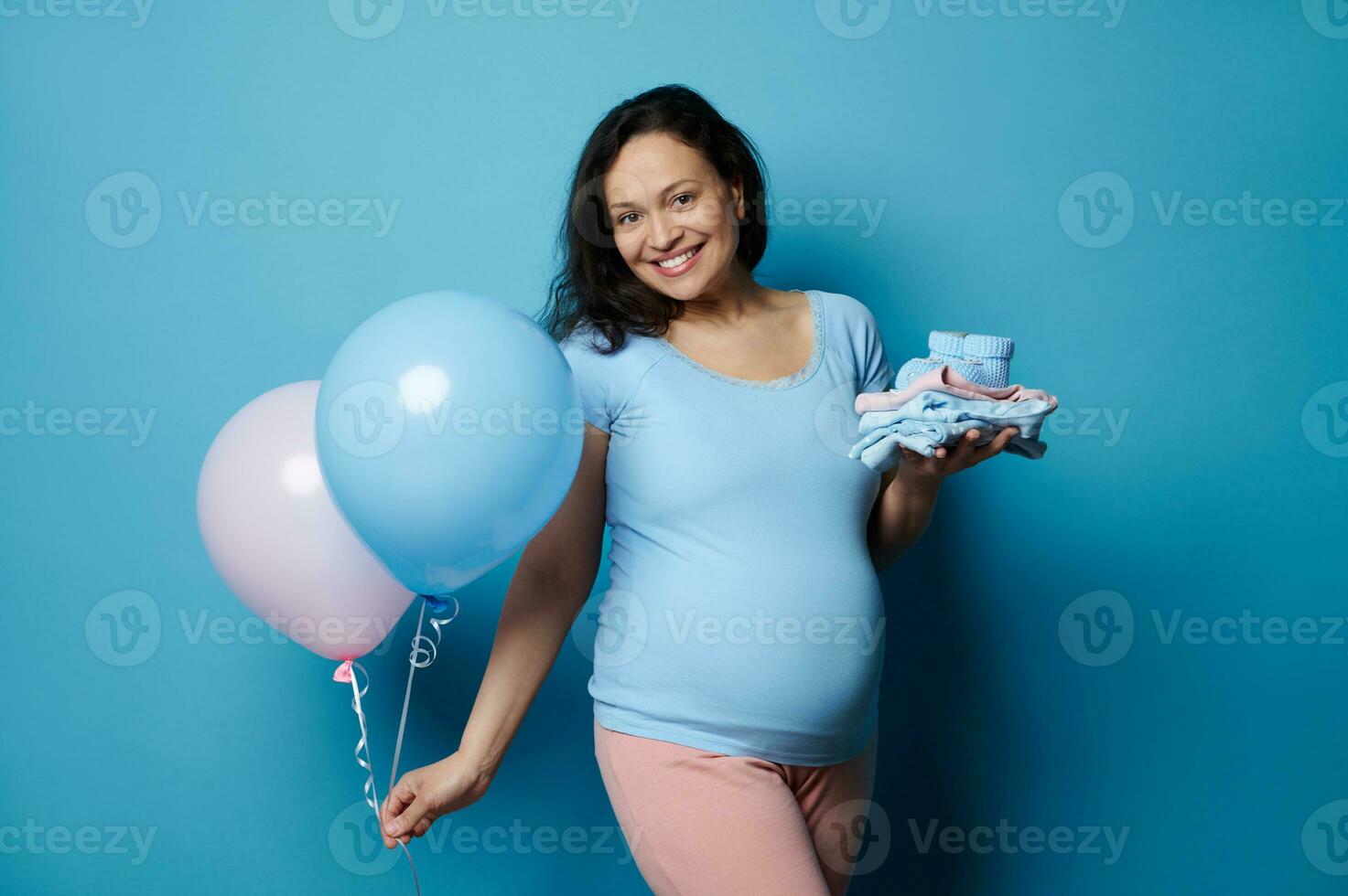 grávida sorridente mulher segurando recém-nascido roupas e dois balões do Rosa e azul cor. gênero revelar festa conceito foto
