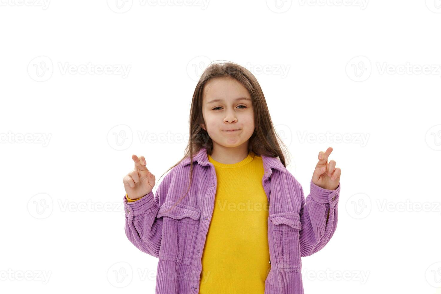 agradável pequeno criança menina com posando com cruzado dedos, esperanças para Boa sorte e dela sonhos venha verdadeiro, branco fundo. foto