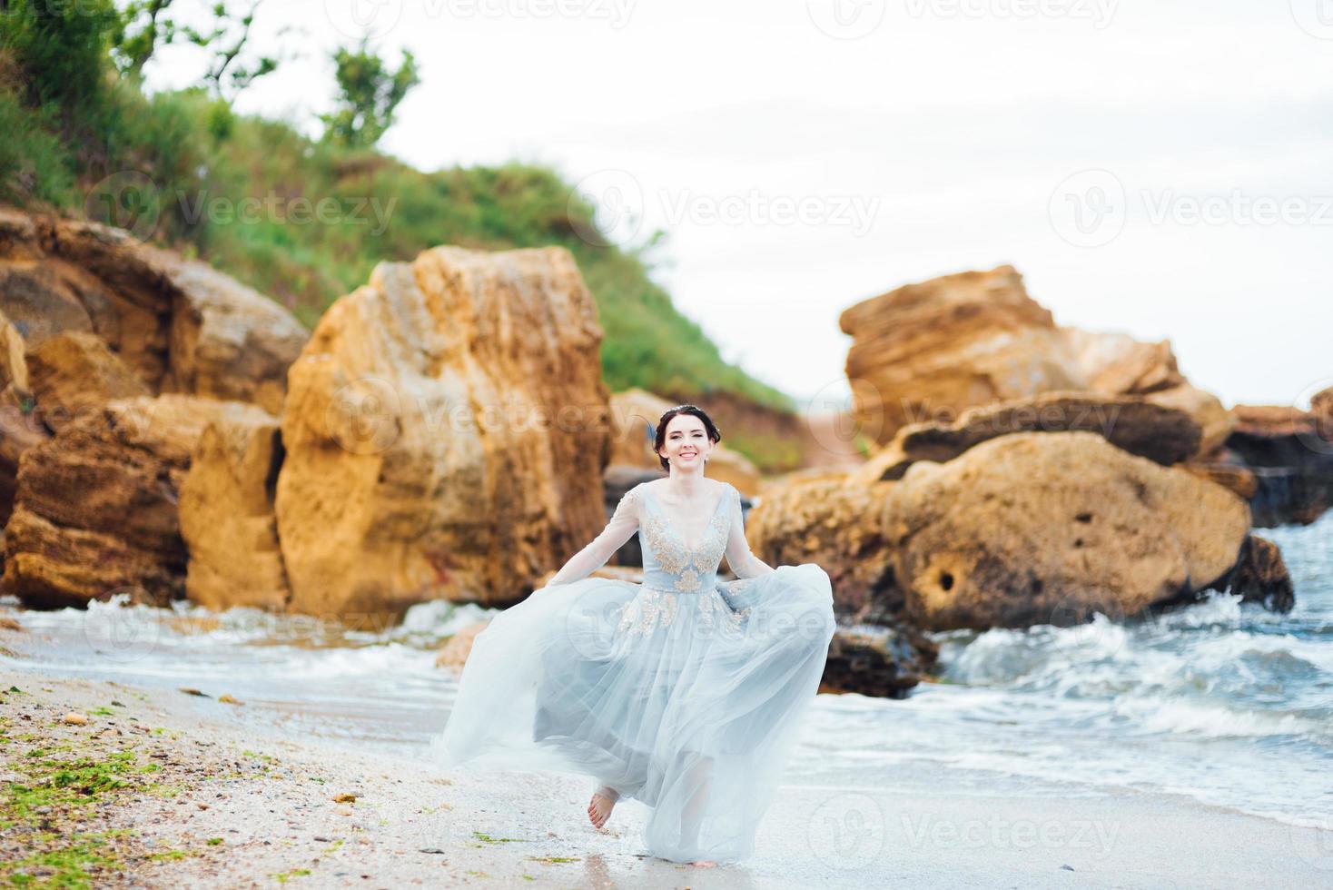 noiva em um vestido azul claro caminhando à beira-mar foto