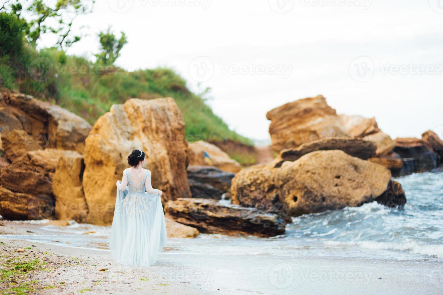 noiva em um vestido azul claro caminhando à beira-mar foto