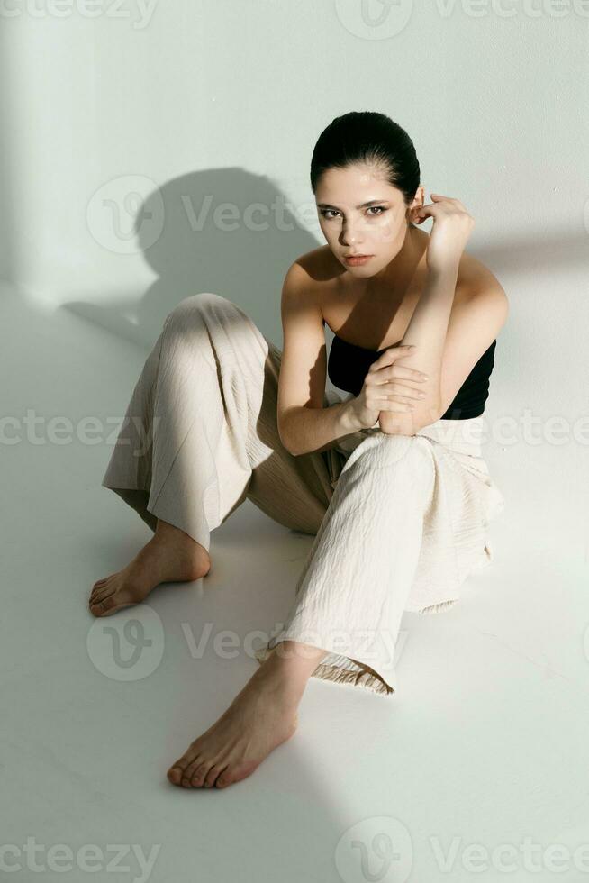 descalço mulher sentado em a chão inclinado contra a parede dentro de casa calça estilo terno foto