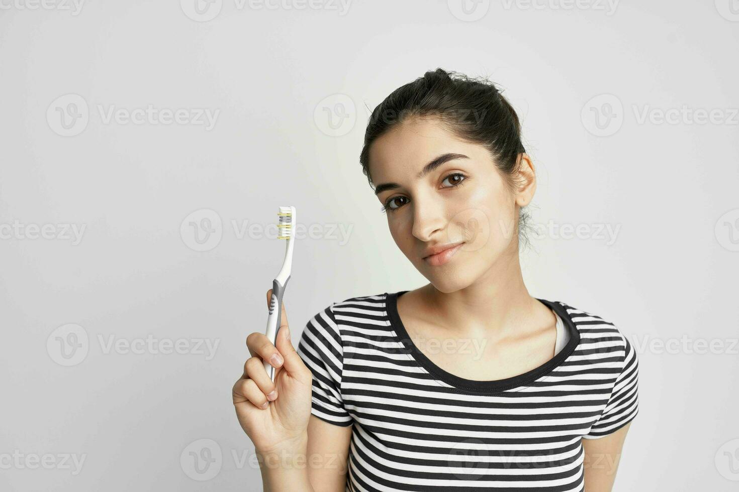 mulher dentro uma listrado camiseta escova de dente dentro mão luz fundo foto