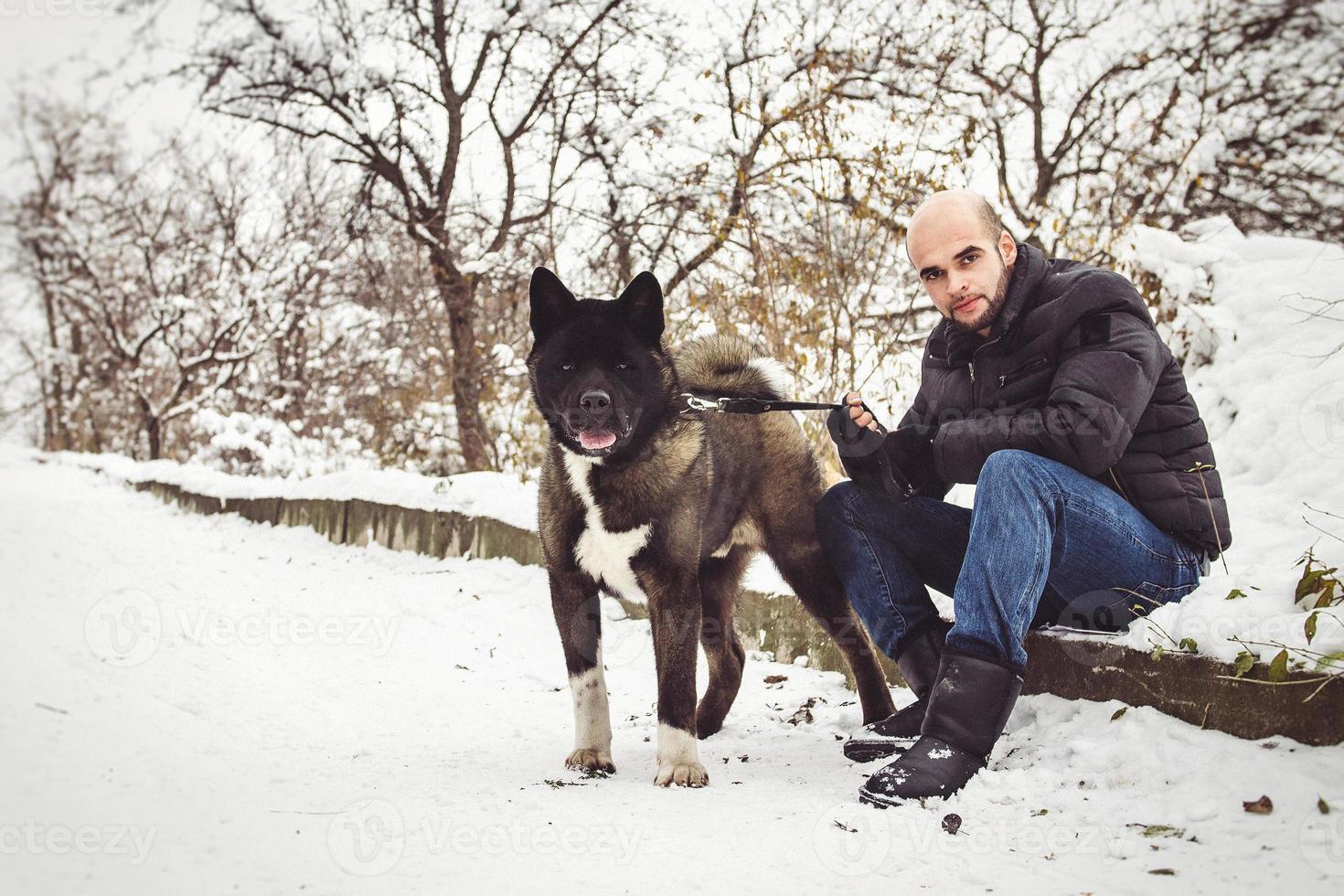 um homem com uma jaqueta e um chapéu de malha caminhando com um cachorro akita americano foto