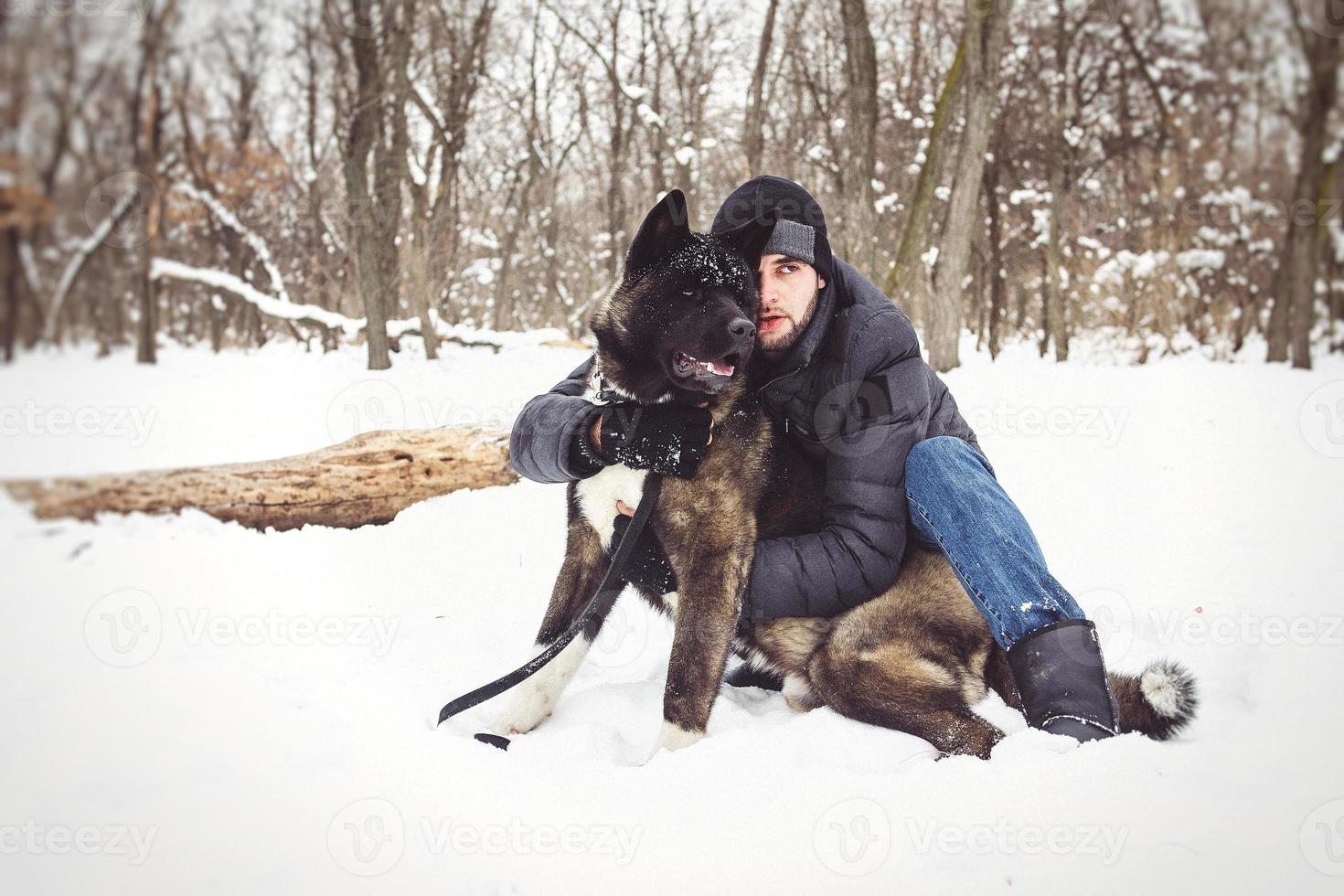 um homem com uma jaqueta e um chapéu de malha caminhando com um cachorro akita americano foto