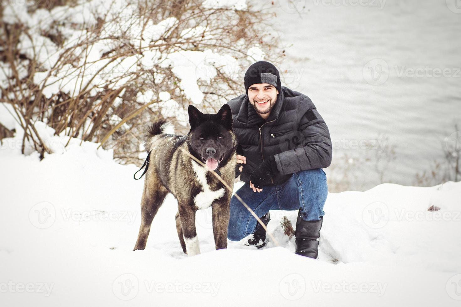um homem com uma jaqueta e um chapéu de malha caminhando com um cachorro akita americano foto