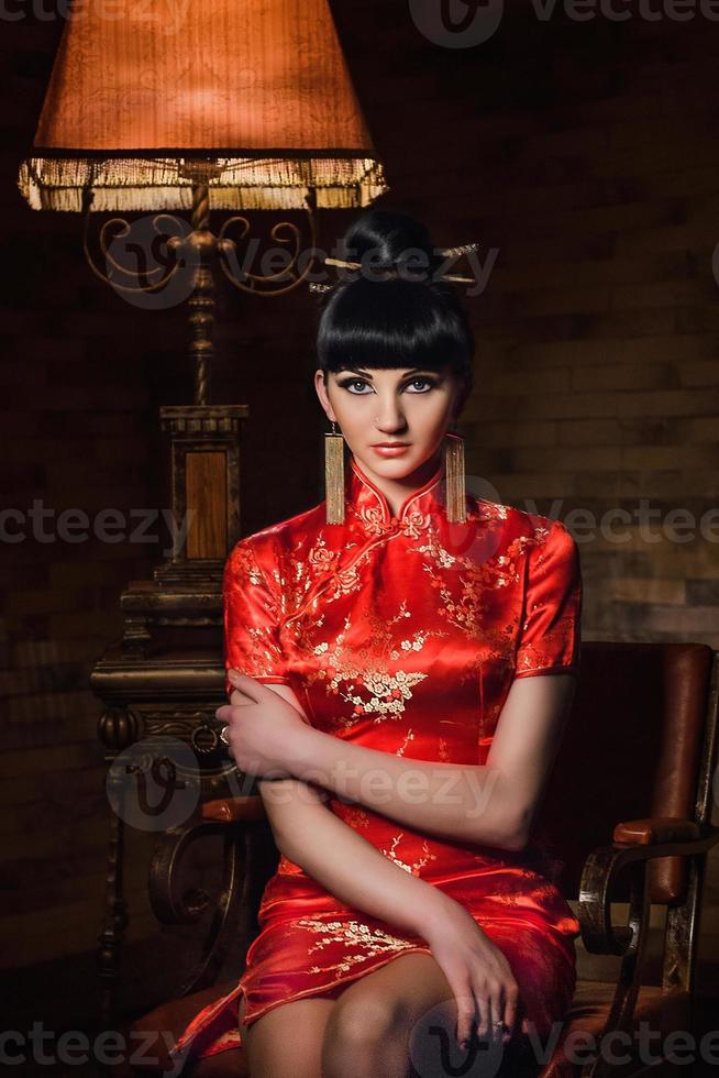 garota em um vestido de seda japonesa vermelha qipao em um quarto escuro foto