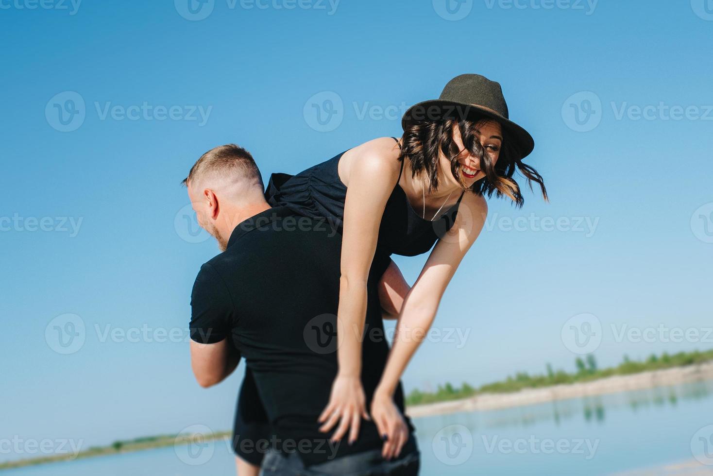 jovem casal um cara com uma garota em roupas pretas está andando na areia branca foto