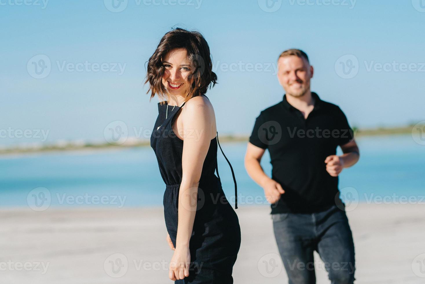 jovem casal um cara com uma garota em roupas pretas está andando na areia branca foto