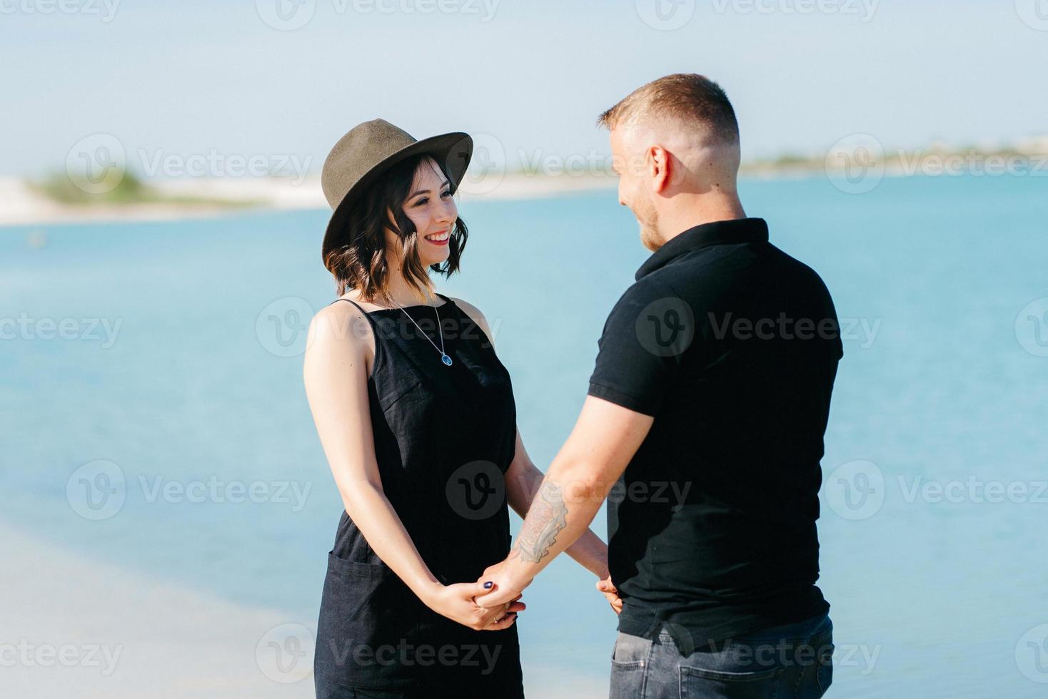 jovem casal um cara com uma garota em roupas pretas está andando na areia branca foto