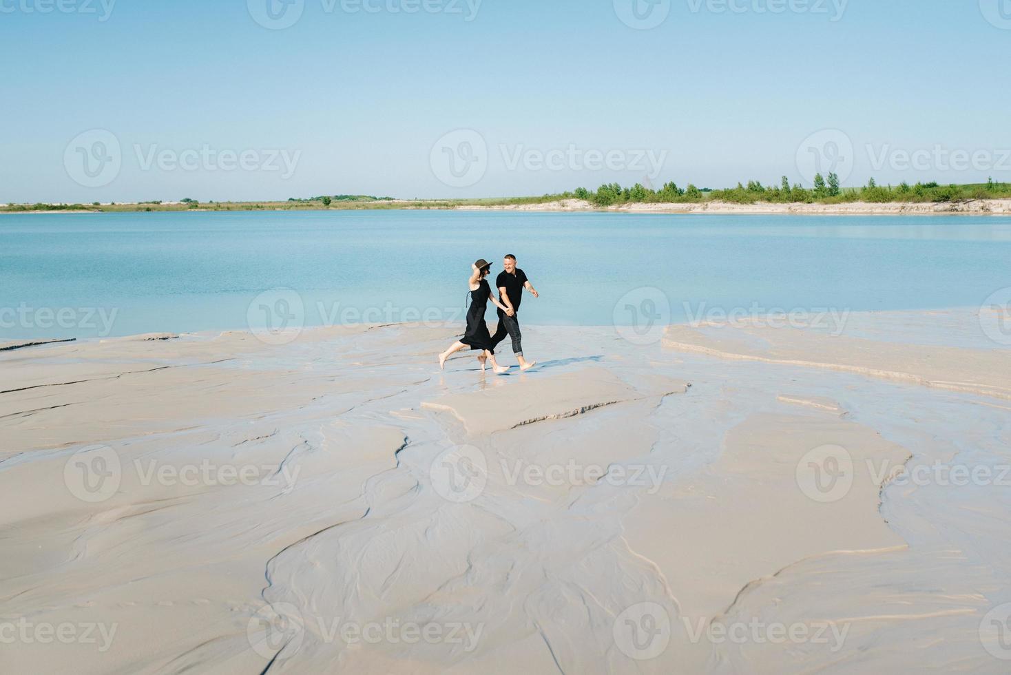 jovem casal um cara com uma garota em roupas pretas está andando na areia branca foto