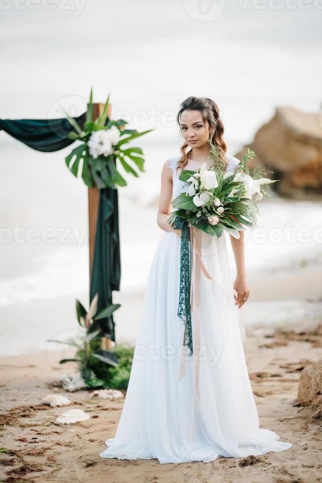 noiva com um buquê de casamento na costa do mar foto