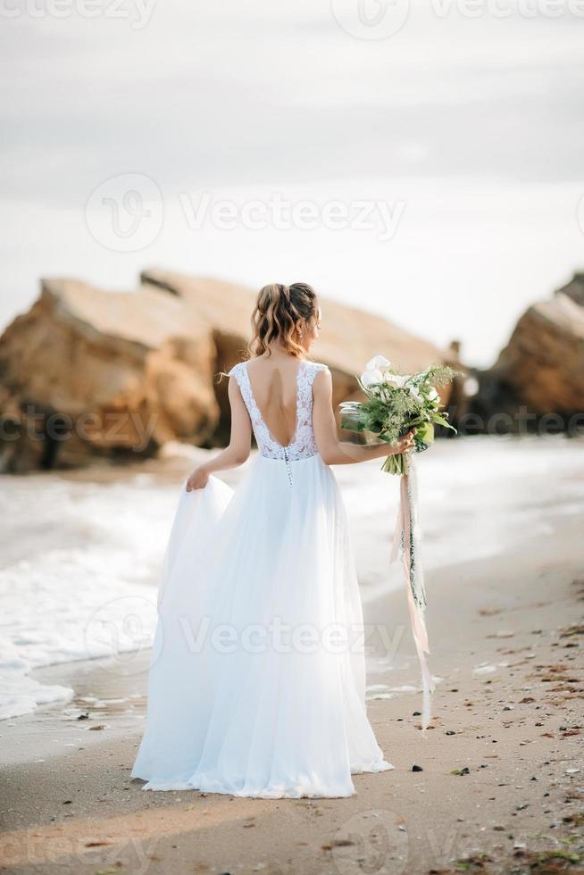noiva com um buquê de casamento na costa do mar foto