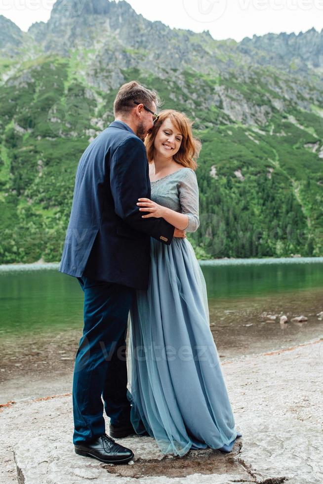 jovem casal passeando perto de um lago cercado por montanhas foto