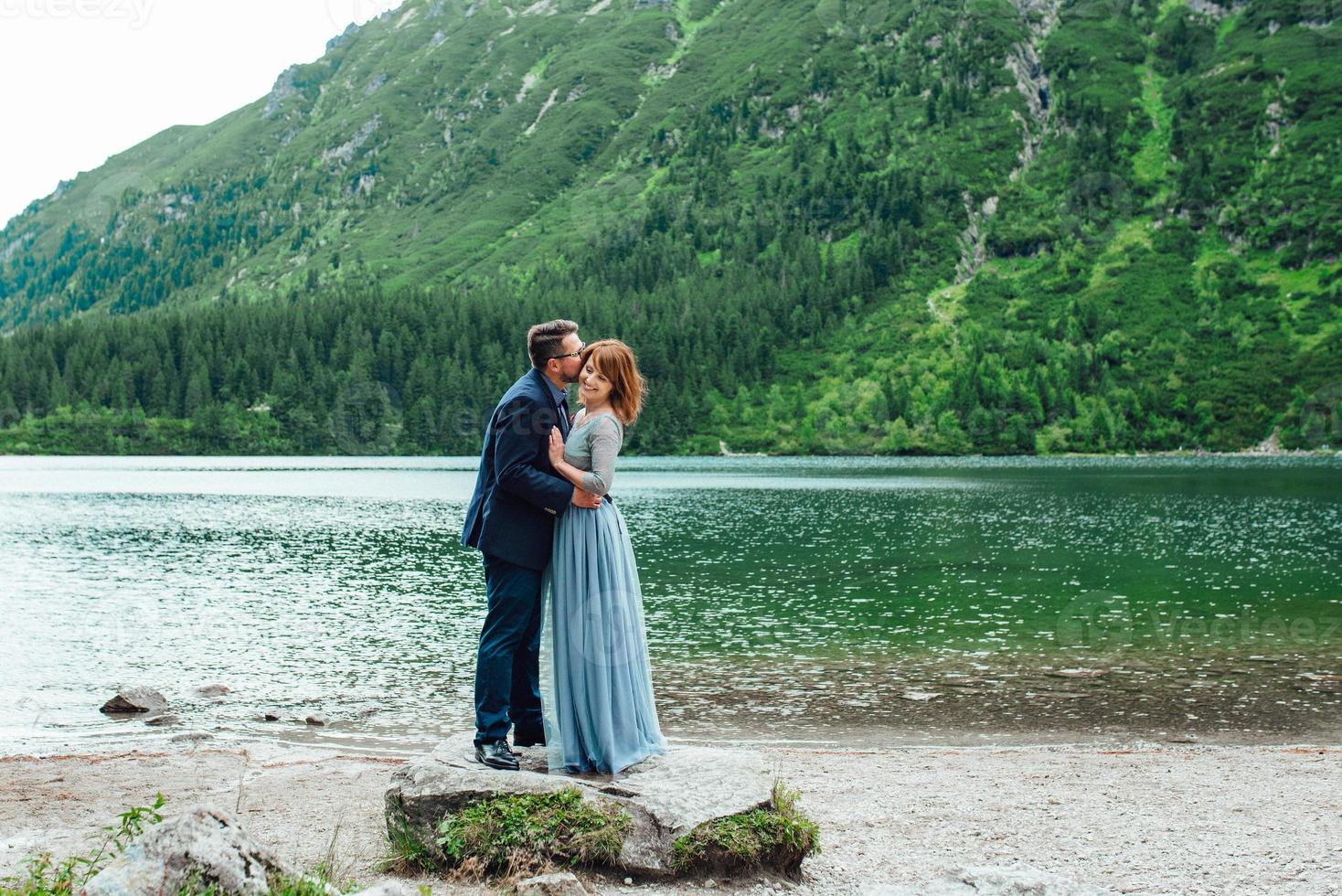 jovem casal passeando perto de um lago cercado por montanhas foto