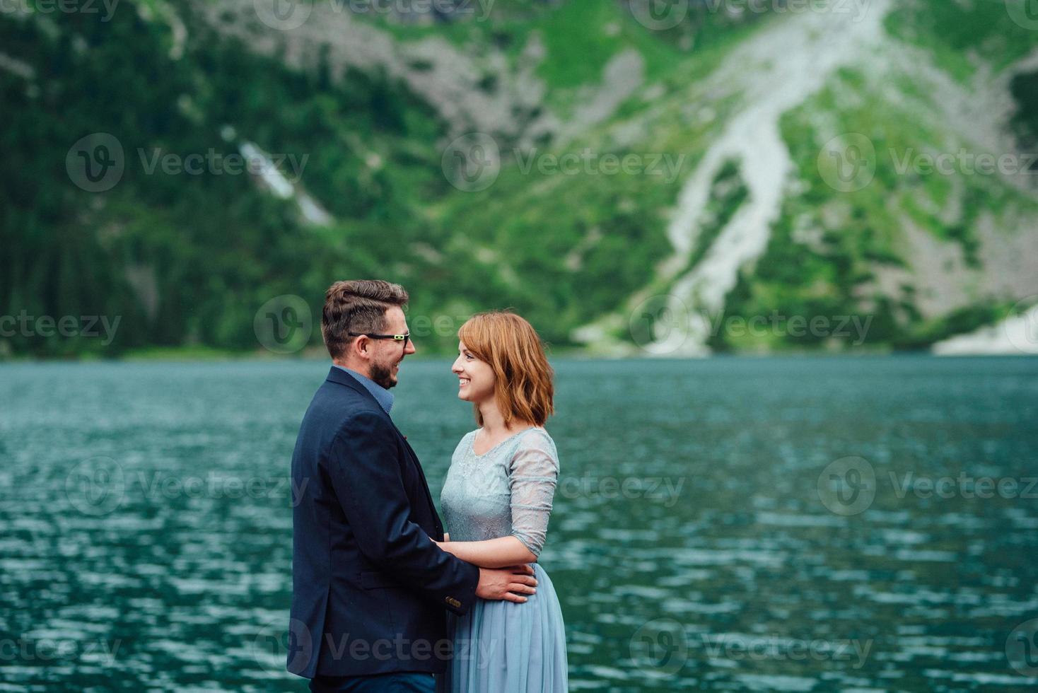 jovem casal passeando perto de um lago cercado por montanhas foto