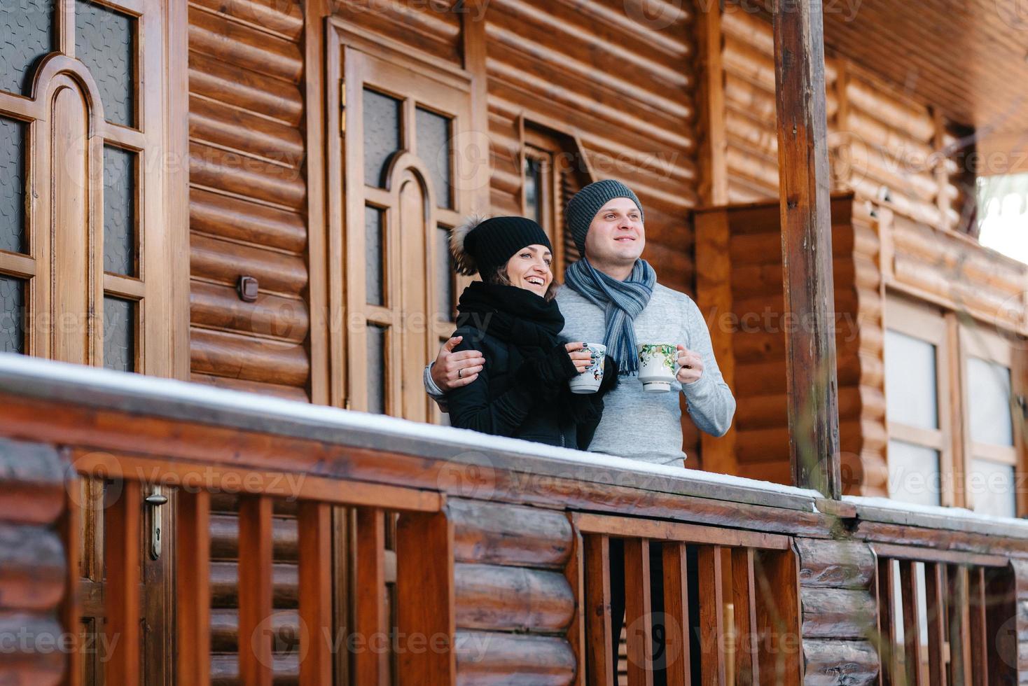 casal de jovens, um cara e uma garota na varanda de uma casa de madeira coberta de neve foto
