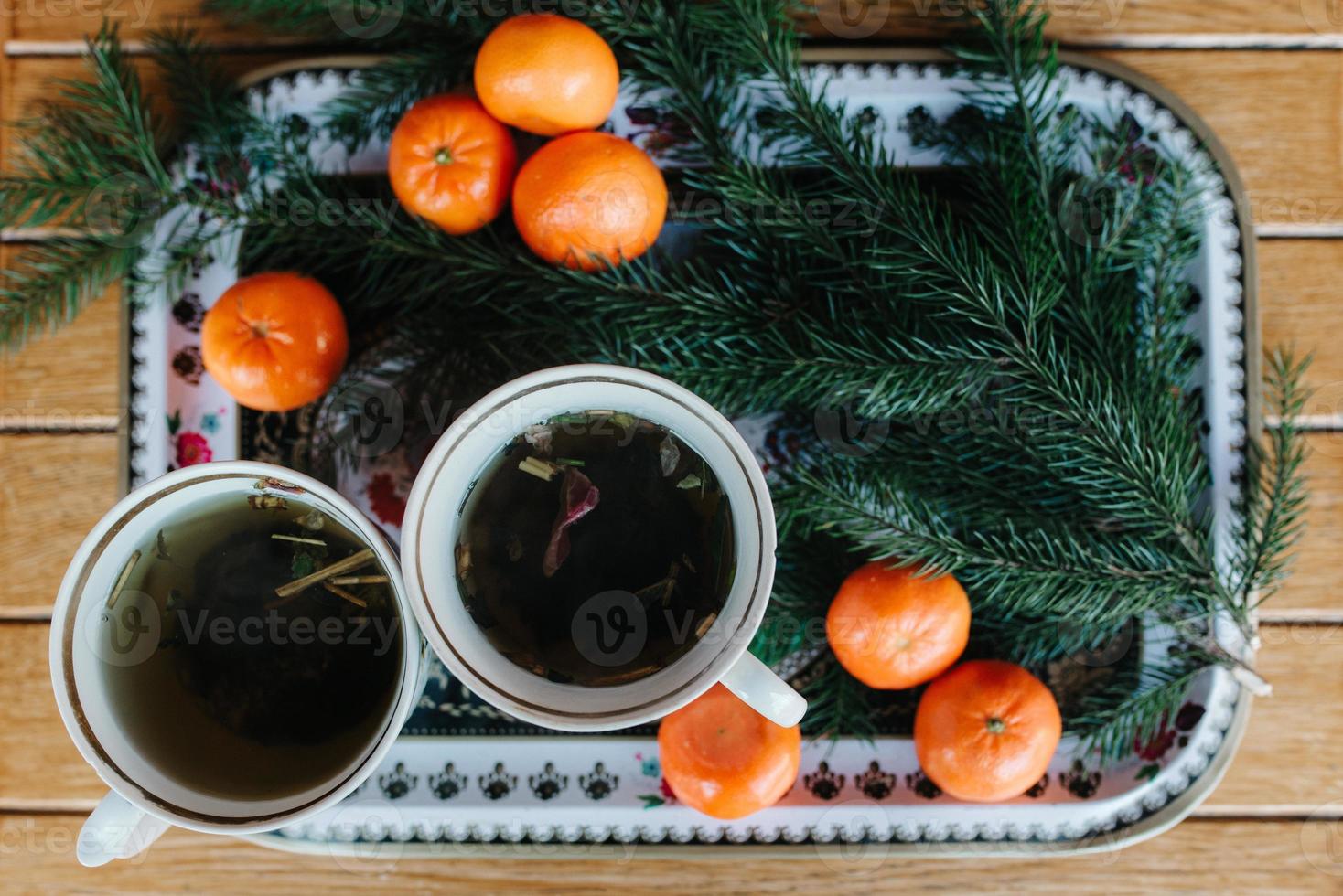duas xícaras de chá de ervas em uma mesa com tangerinas e um galho de abeto foto