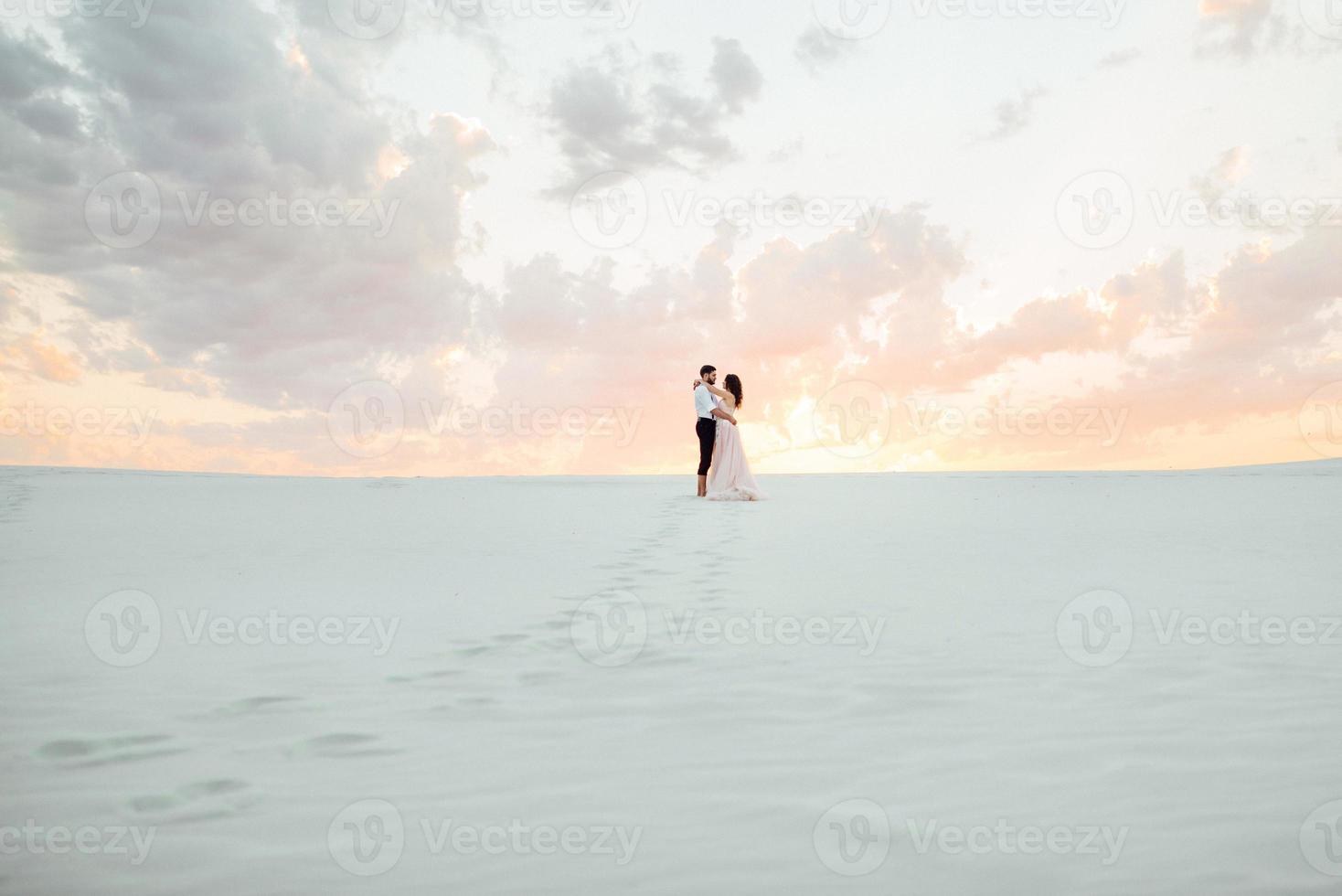 casal jovem um cara de calça preta e uma garota de vestido rosa estão caminhando na areia branca foto