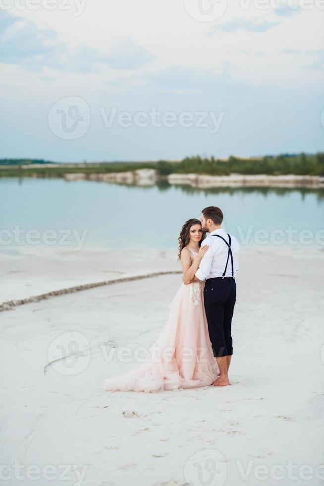 casal jovem um cara de calça preta e uma garota de vestido rosa estão caminhando na areia branca foto