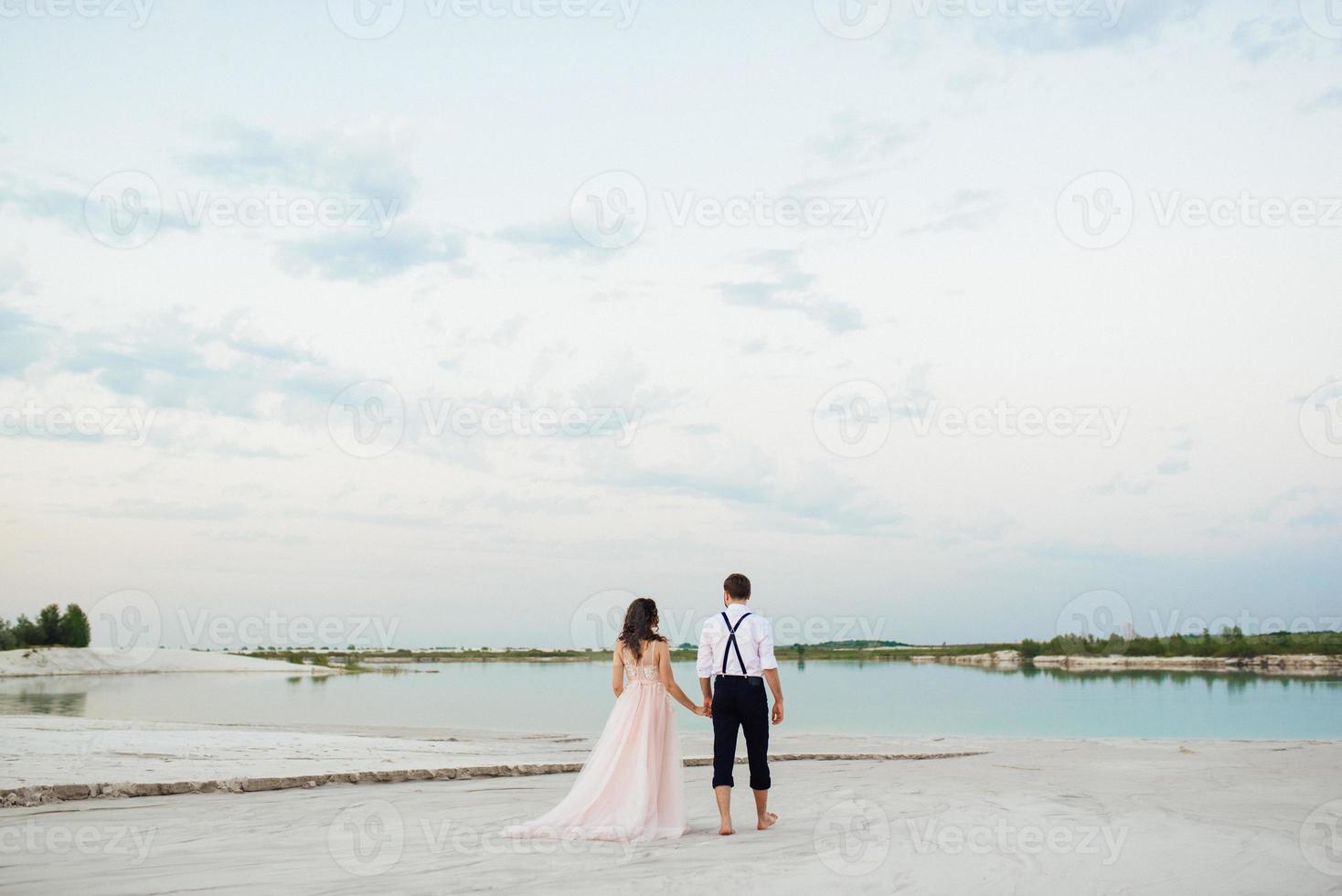 casal jovem um cara de calça preta e uma garota de vestido rosa estão caminhando na areia branca foto