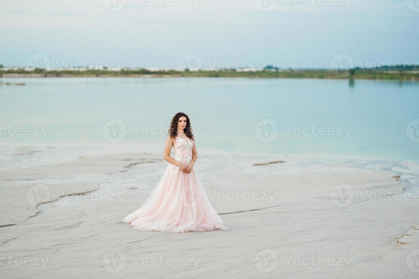 garota de vestido rosa está andando na areia branca foto