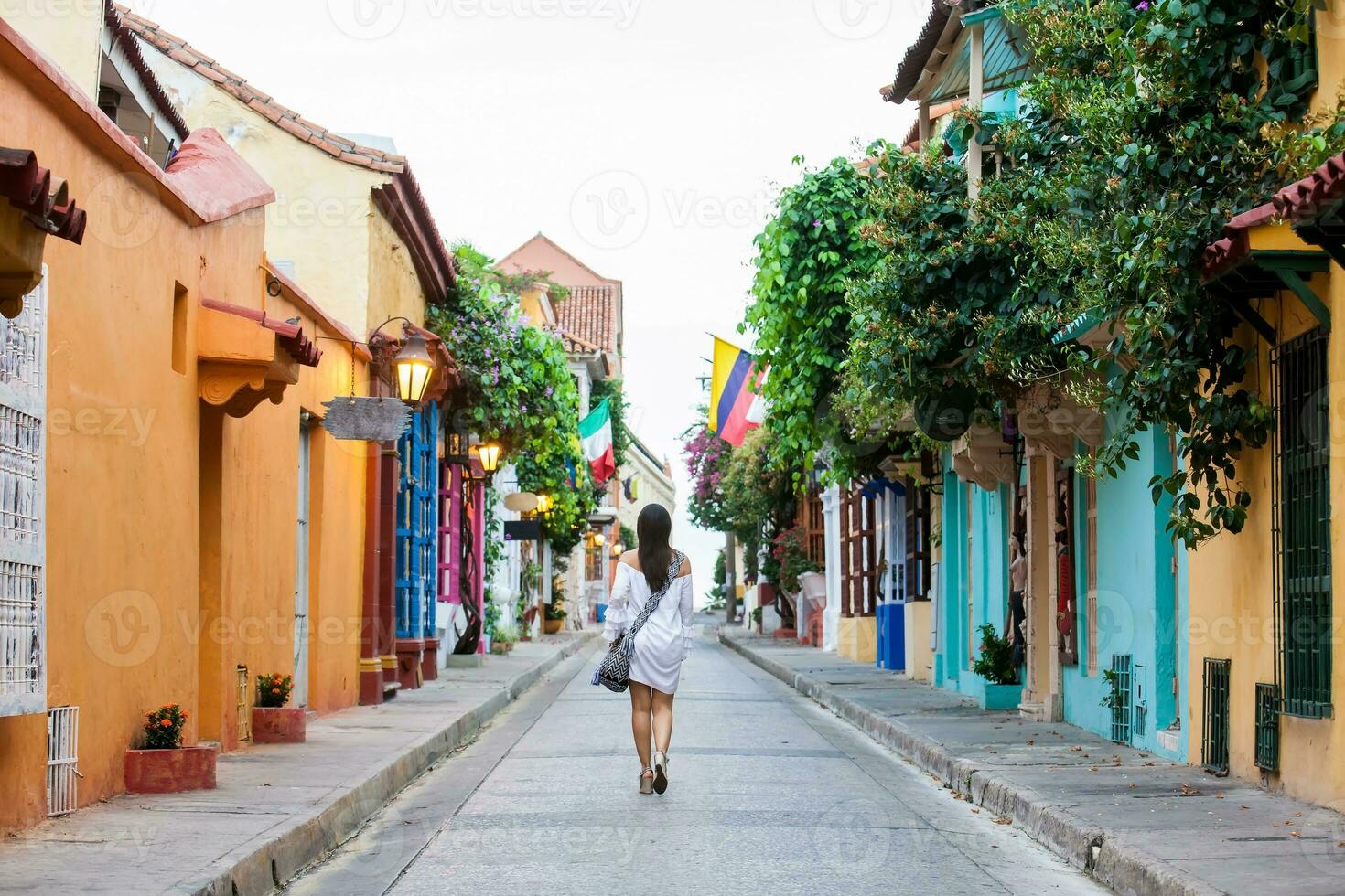 lindo mulher em branco vestir caminhando sozinho às a colorida ruas do a colonial murado cidade do cartagena de índias foto