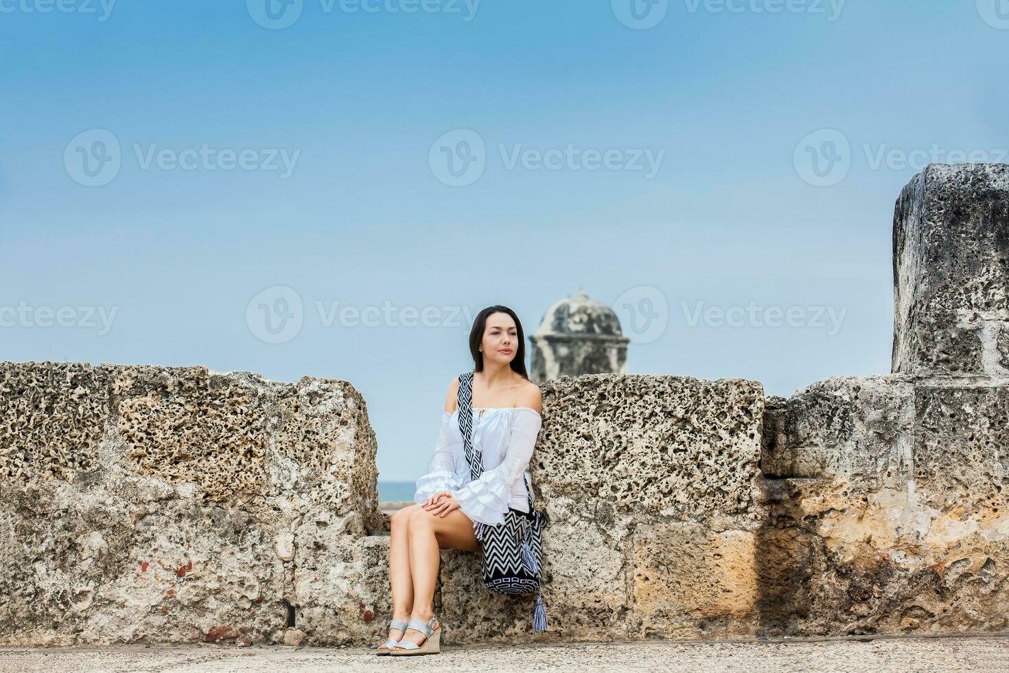 lindo mulher em branco vestir sentado sozinho às a paredes em torno da a colonial cidade do cartagena de índias foto