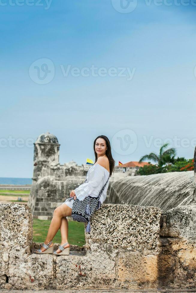 lindo mulher em branco vestir sentado sozinho às a paredes em torno da a colonial cidade do cartagena de índias foto
