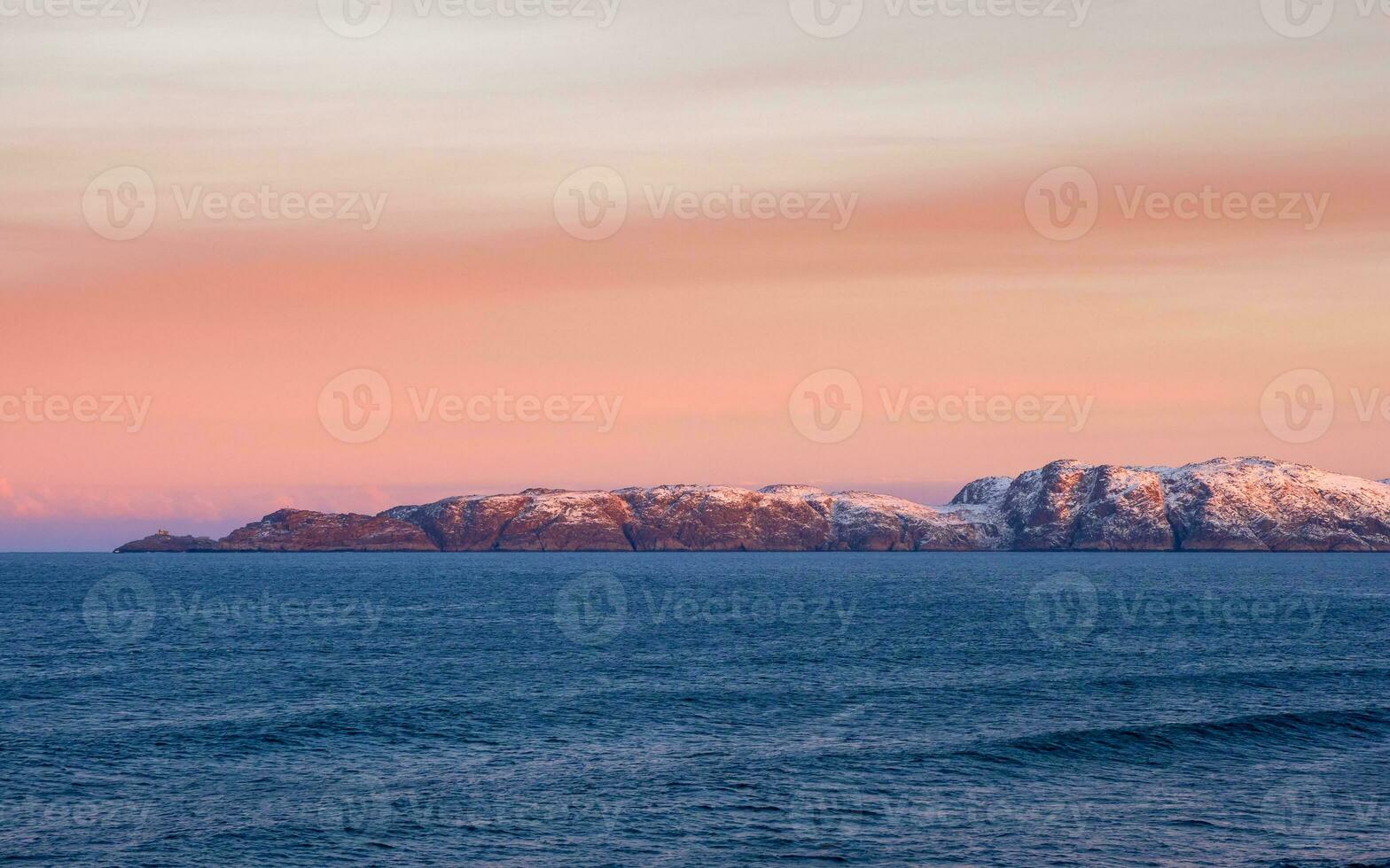 lindo Rosa pôr do sol em a ártico oceano. uma Península com coberto de neve colinas em a horizonte. mar minimalista panorama. foto