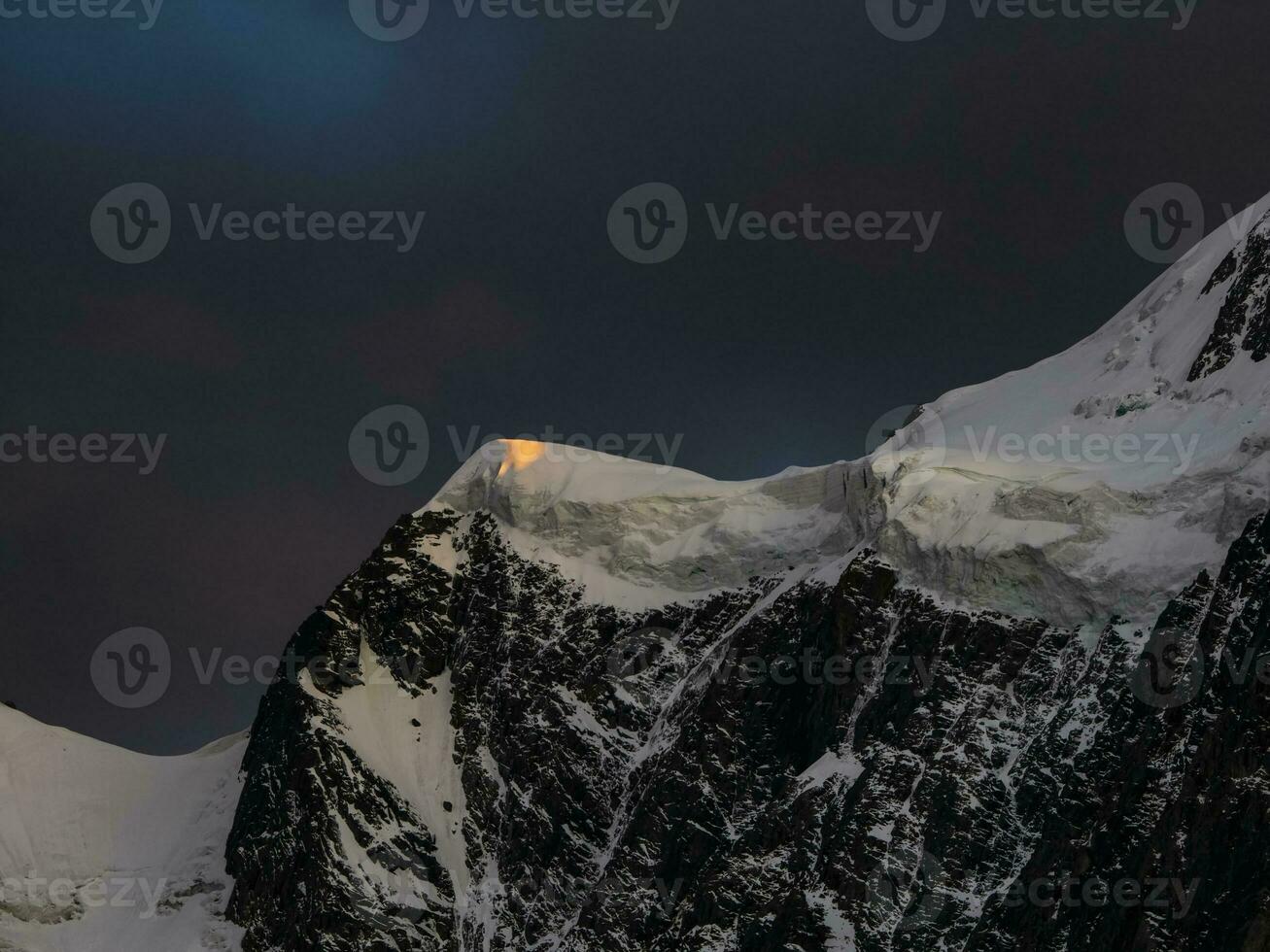 Trevas montanha panorama com ótimo Nevado montanha aceso de alvorecer Sol entre Sombrio nuvens. impressionante alpino cenário com Alto montanha pináculo às pôr do sol ou às nascer do sol. grande geleira em topo dentro laranja claro. foto