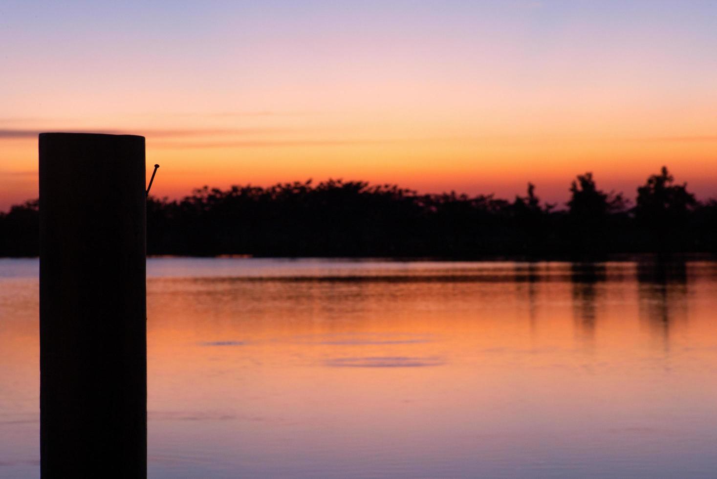 silhueta de prego no poste de madeira no cais com o lago e o céu do pôr do sol no fundo foto