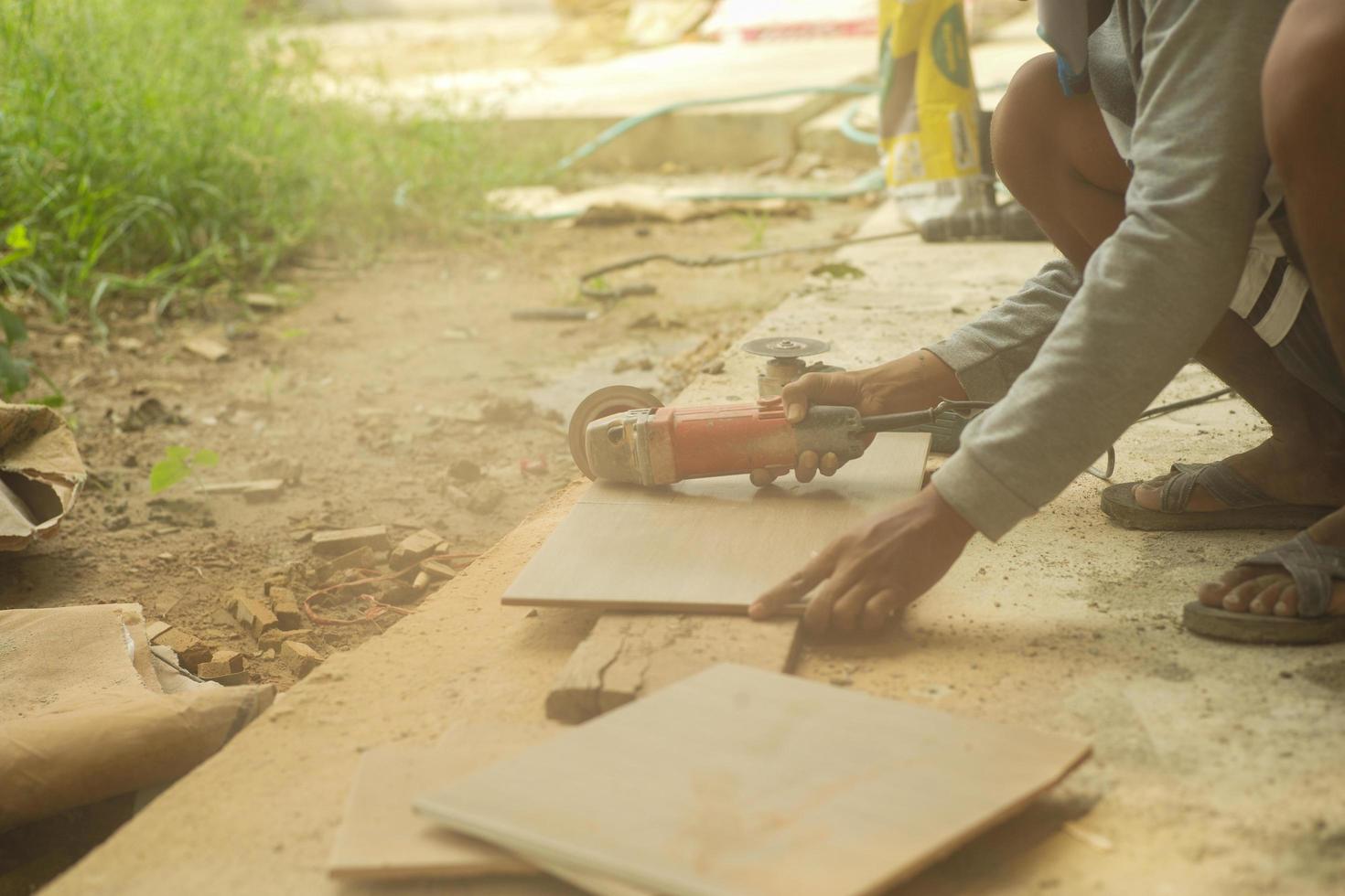 trabalhador que corta o ladrilho pela máquina de corte elétrica no canteiro de obras com nuvem de poeira no ambiente. foto