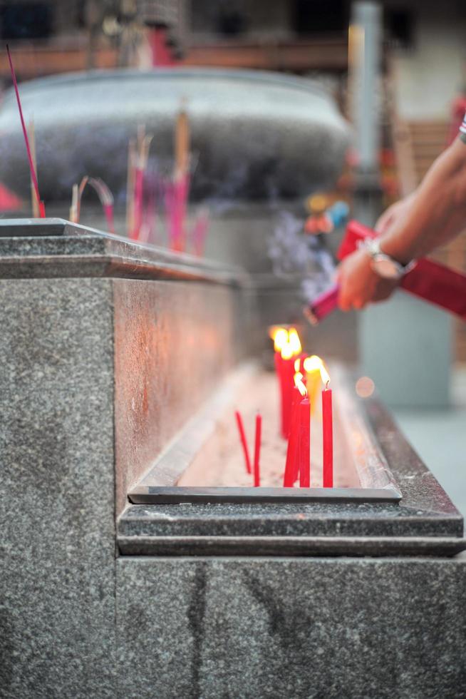 grupo de velas vermelhas colocadas na areia em uma bandeja de concreto com mãos borradas segurando incensos foto