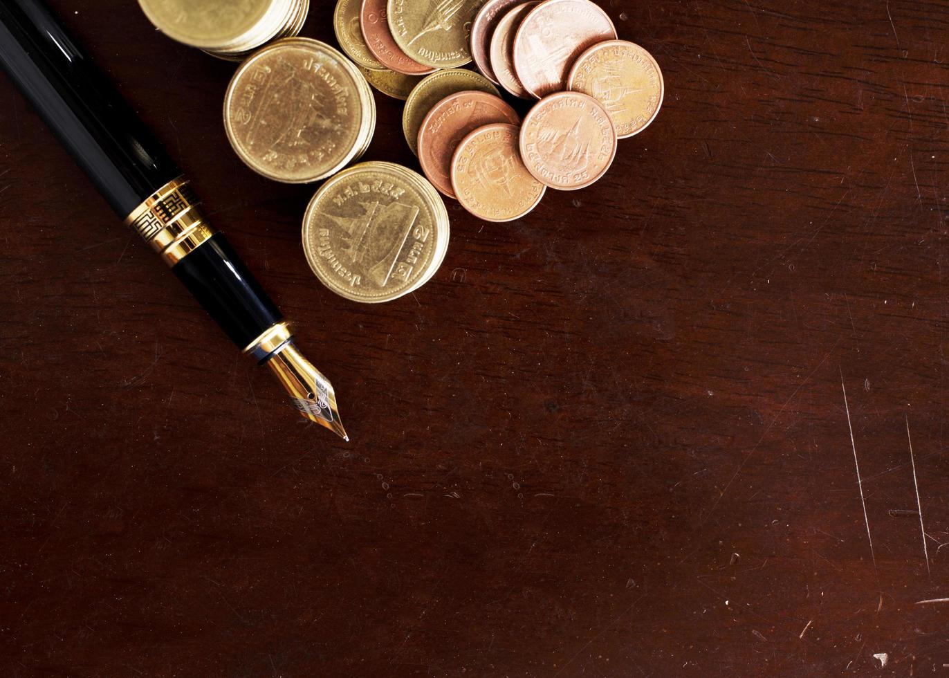 Caneta-tinteiro e moedas de dinheiro empilhadas na mesa de madeira para o fundo do conceito de finanças. foto