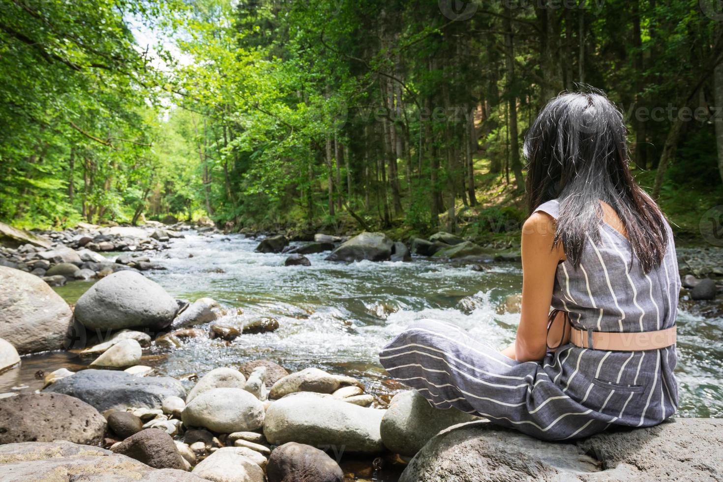 mulher sentada em uma pedra olhando para um rio foto