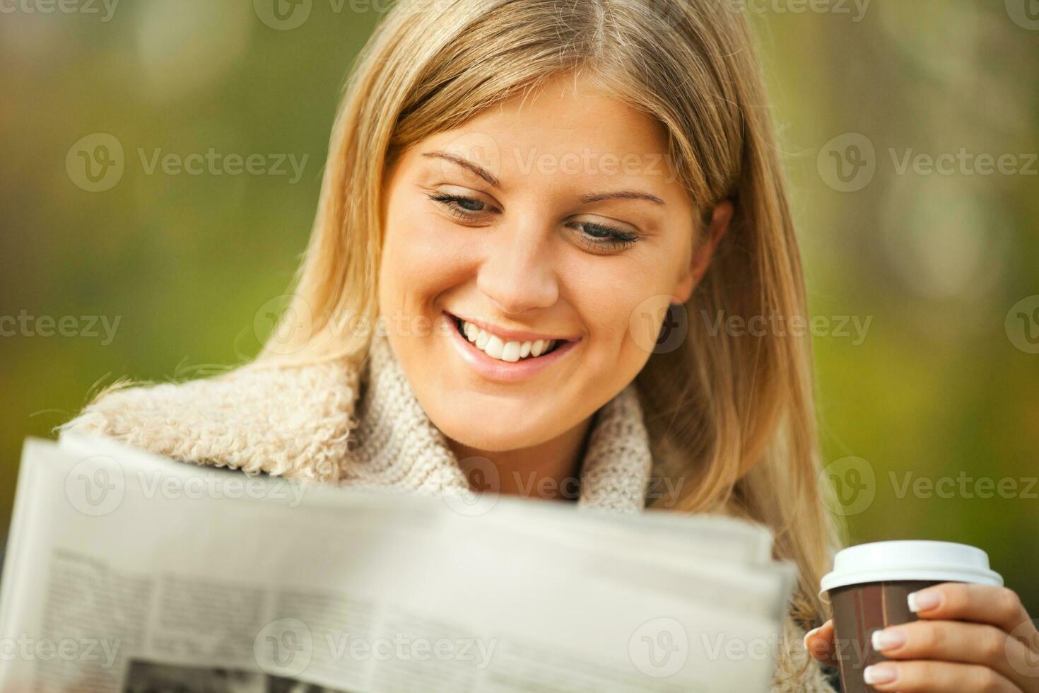 uma mulher tendo café dentro a parque e lendo uma jornal foto