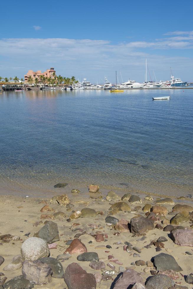 malecón de la paz na baja califórnia sur méxico com pedras na praia e embarcações náuticas no fundo do céu azul e manhã ensolarada com mar calmo foto