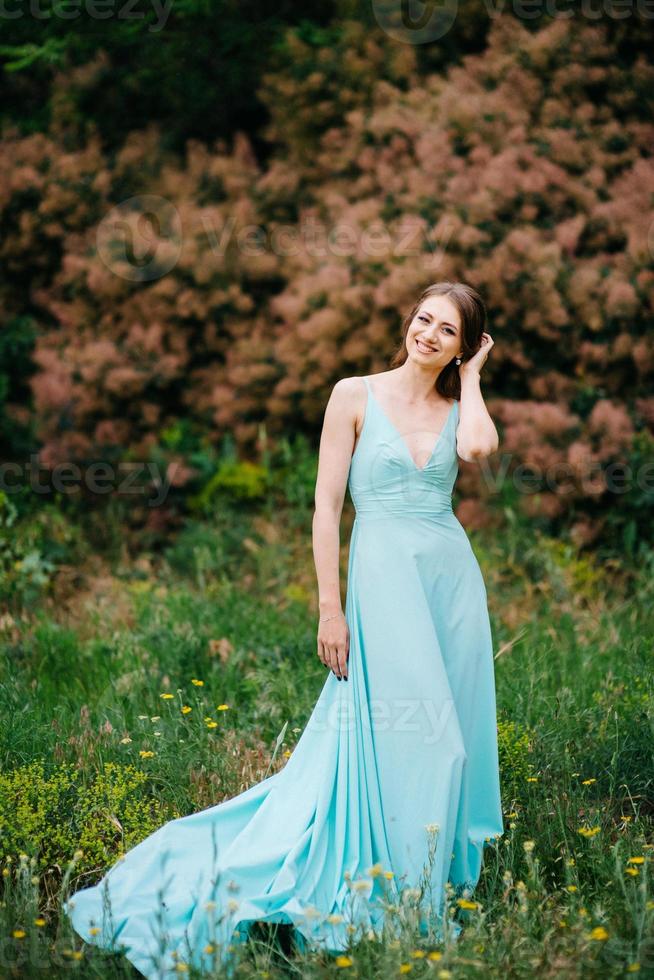 garota feliz em um vestido longo turquesa em um parque verde foto