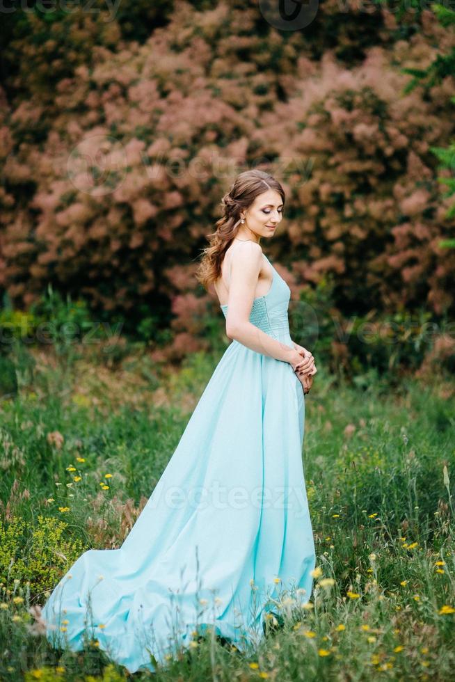 garota feliz em um vestido longo turquesa em um parque verde foto