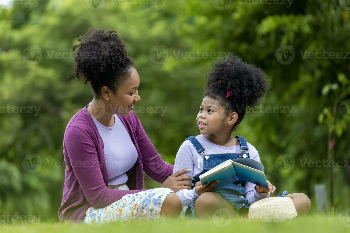 africano americano mãe é ensino dela jovem filha para ler enquanto tendo uma verão piquenique dentro a público parque para Educação e felicidade foto