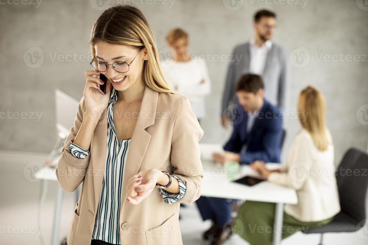 mulher falando ao telefone com colegas de trabalho ao fundo foto