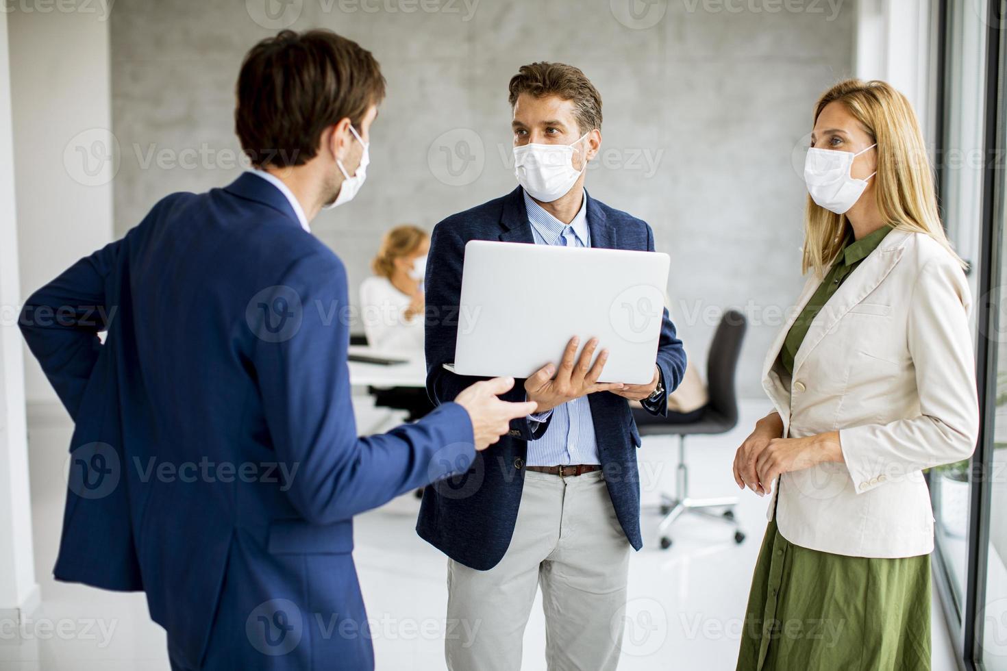 três profissionais mascarados conversando com laptop foto