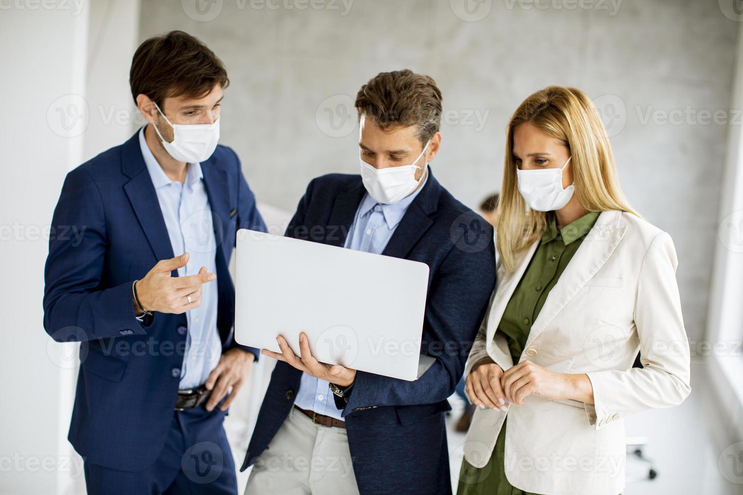 três profissionais mascarados olhando para um laptop foto