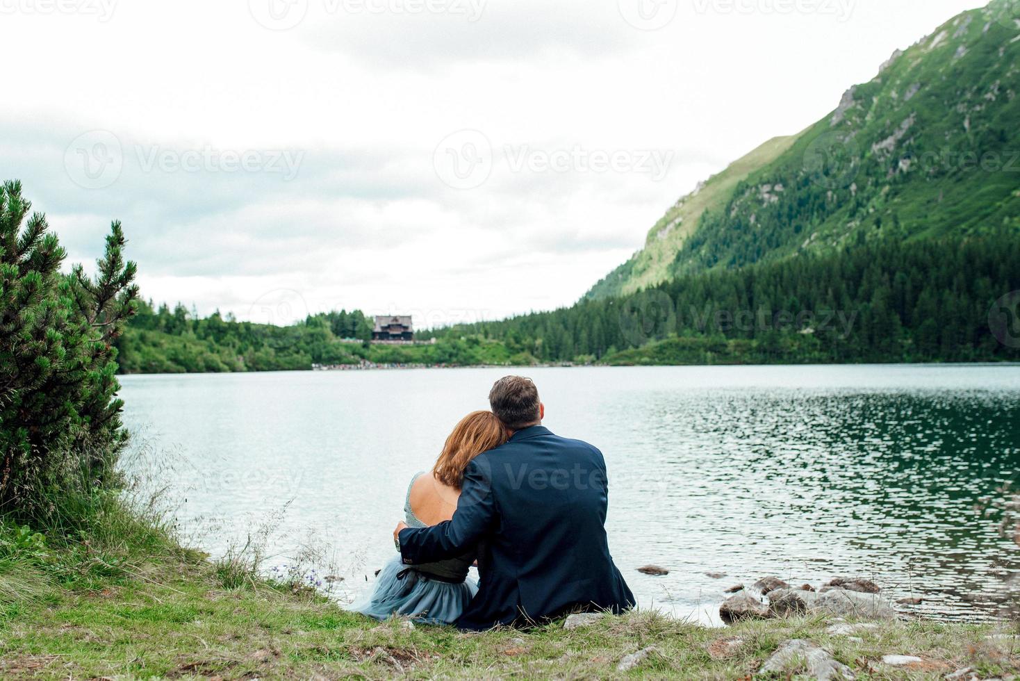 jovem casal passeando perto de um lago cercado por montanhas foto