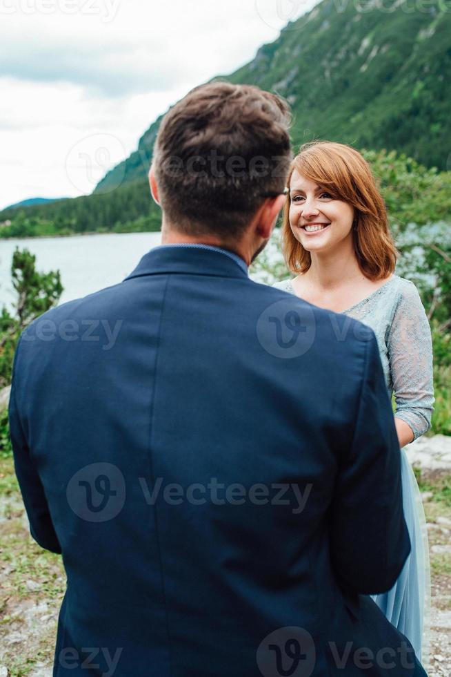 jovem casal passeando perto de um lago cercado por montanhas foto