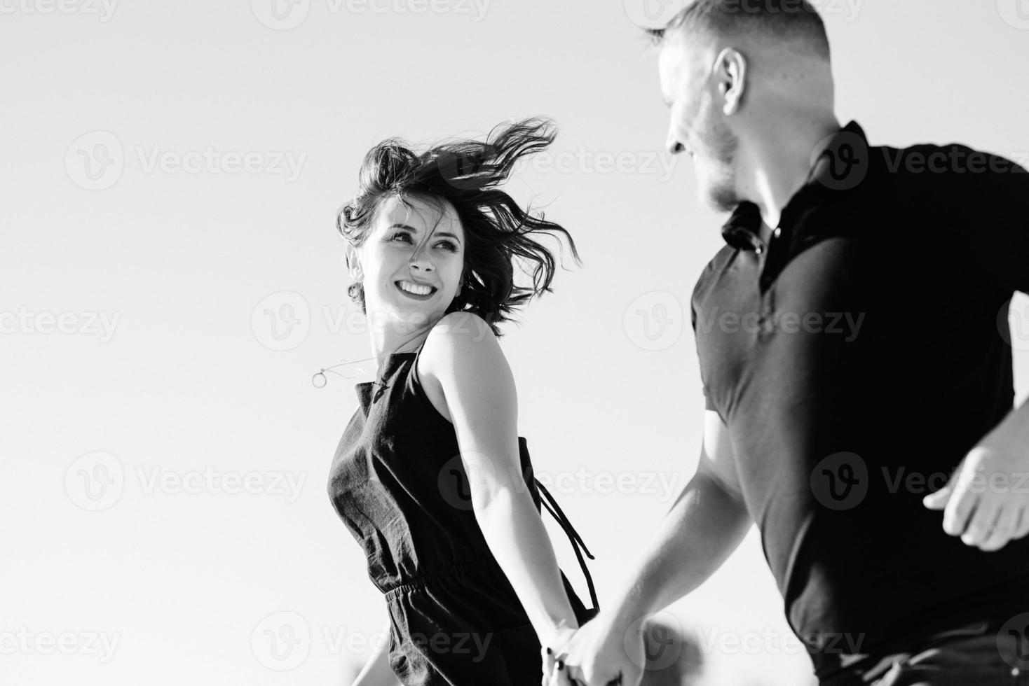 jovem casal um garoto e uma garota com emoções alegres em roupas pretas caminham pelo deserto branco foto